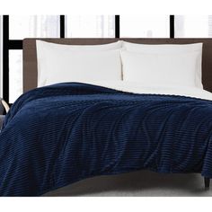 a bed with blue and white comforter on it in front of large black windows