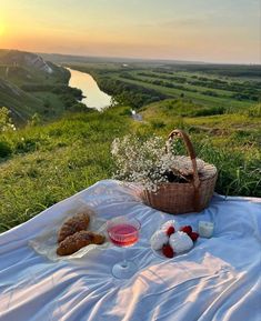 a picnic blanket on the grass with food and wine in front of it, overlooking a river