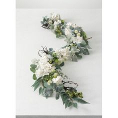 two white flowers and greenery are arranged on a table top, with the letter e in the middle