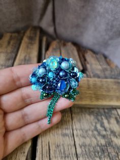 a person is holding a brooch with pearls and blue beads on it's finger