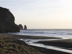 two people walking on the beach near some cliffs