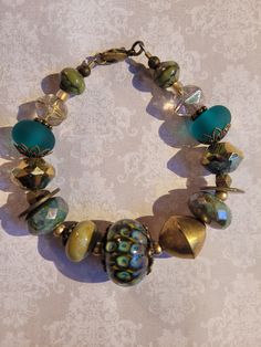 "Gorgeous teal and green glass bracelet with bronze finish findings. 7.25\", chunky beads." Handmade Bronze Bracelets With Round Beads, Unique Turquoise Czech Glass Beaded Bracelets, Green Brass Bracelet As Gift, Handmade Green Brass Bracelets, Handmade Brass Bracelets In Green, Handmade Green Brass Bracelet, Bohemian Turquoise Glass Bracelets, Green Brass Bracelet Jewelry, Green Brass Bracelet