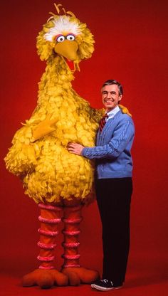 a man standing next to a big bird in front of a red background with his arms around him