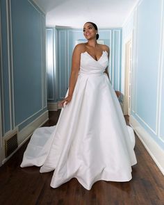 a woman in a white wedding dress standing on a wooden floor next to a blue wall