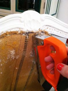 a person holding an orange object in front of a white headboard with peeling paint on it