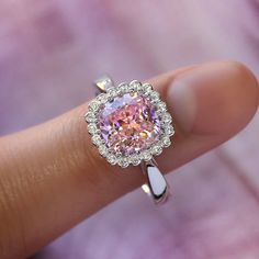 a close up of a person's hand holding a ring with a pink diamond in it