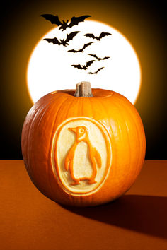 a pumpkin carved to look like a penguin with bats coming out of it and the moon in the background