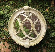 a circular mirror hanging on the side of a brick wall with ivy growing around it