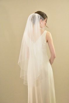 a woman in a white dress is wearing a veil and looking at the back of her head