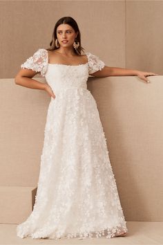 a woman in a white wedding dress leaning against a wall with her arms out and looking at the camera