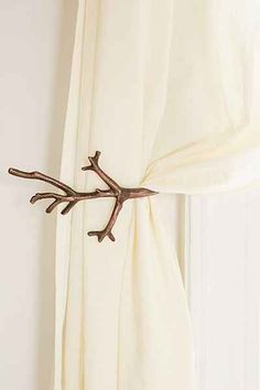 a branch is mounted on the curtain rod in front of a window with white drapes