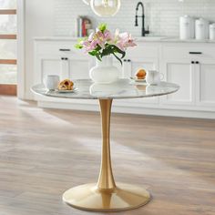 a white vase with pink flowers sitting on top of a marble table in a kitchen