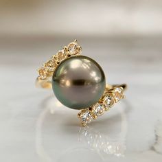 Lovely Tahitian Pearl bypass ring with white topaz accents.  This is a brand new piece. No issues to note.  Hallmarked and tested. Band is a 7.25 and sizable upon request for an additional charge. We are a brick and mortar store located in Alhambra, CA. All items are guaranteed as described. SPECIFICATIONS: Size: 7.25 Pearl: 9.7mm Weight: 4.3 Grams     This ring has been inspected by professionals with over 35 years of experience to ensure its excellent condition. **Please inquire about sizing before purchase or making an offer. Order will ship within 24 hours. We offer a 14-day, no-questions-asked return policy.  Please see detailed pictures, as they are part of the description, and do not hesitate to contact us should you have any questions.  Thank you and happy shopping! Luxury White Gold Tahitian Pearl Ring, Luxury Tahitian Pearl Classic Ring, Luxury Fine Jewelry Tahitian Pearl Rings, Topaz Cocktail Ring, Tahitian Pearl Ring, Beautiful Diamond Earrings, Pearl Necklace Designs, Bypass Ring, Cabochon Ring