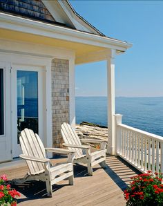 two white adiron chairs sitting on top of a wooden deck next to the ocean