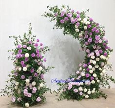 two purple and white flowers are arranged in the shape of an arch with greenery