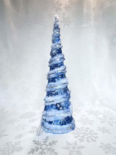 a blue glass christmas tree sitting on top of a white table covered in snowflakes