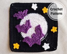 a crocheted square with purple and white flowers on it, sitting on top of a table