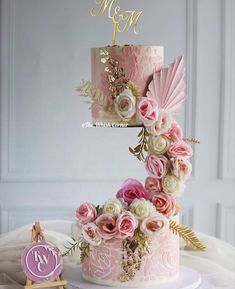 a three tiered cake with pink and white flowers on top, next to a monogram sign