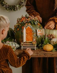 a young boy is decorating a pumpkin house with flowers and greenery on the table