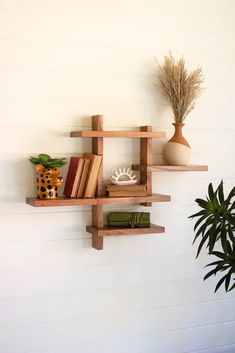 two wooden shelves with books and vases on them against a white wall next to a potted plant