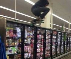 a man on a skateboard jumping over the top of a vending machine in a grocery store