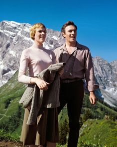 a man standing next to a woman on top of a mountain