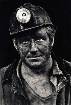 a black and white photo of a man wearing a fireman's hat with a light on his forehead