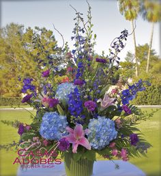 a vase filled with blue and purple flowers on top of a table in front of trees