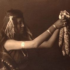 an old photo of a native american woman holding some kind of bird in her hand