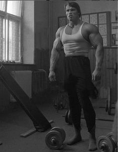 a man standing next to a barbell in a room with lots of equipment on the floor