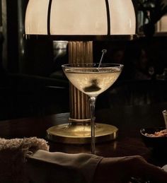 a martini glass sitting on top of a wooden table next to a white lamp shade