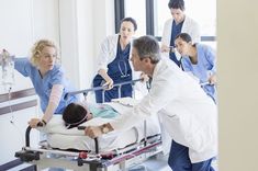 a group of medical personnel standing around a patient in a hospital bed with the nurse pointing at him