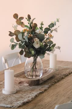 a glass vase filled with flowers on top of a wooden table next to two white candles