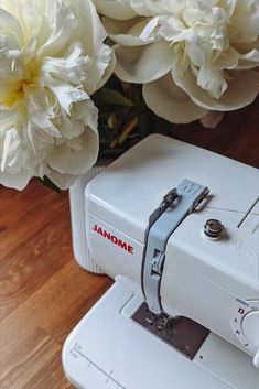 a white sewing machine sitting on top of a wooden floor next to some white flowers