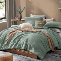 a bed with green comforter and pillows in a room next to a window on the floor