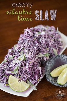 a plate with cabbage slaw and two lime wedges on it, next to a bowl