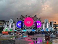 an outdoor stage set up for a concert with multiple colored lights and large screens on it