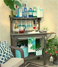 an outdoor bar with bottles and glasses on the top shelf next to potted plants