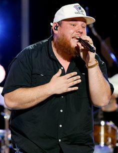 a bearded man singing into a microphone while holding his hands out to the side and wearing a white hat