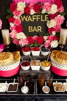 a waffle bar is set up on a table with pink flowers and desserts