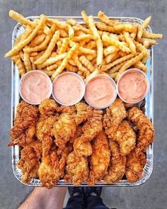 a tray filled with fried chicken and fries next to dipping sauces on the side