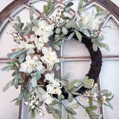 a wreath with white flowers and greenery hanging on a window sill in front of a stained glass door