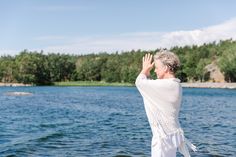 an older woman standing on the edge of a body of water with her hands in the air