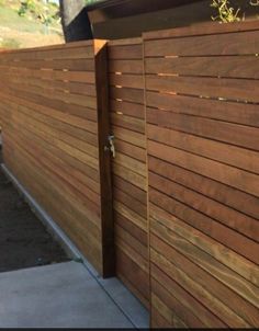 a wooden fence that is next to a sidewalk and some bushes on the side of it