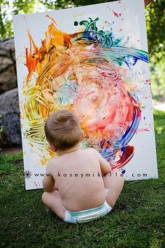 a baby sitting on the grass in front of a painting