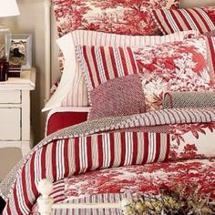 a bed with red and white comforters in a room next to a lamp on a table