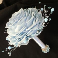 a bridal bouquet with blue flowers and pearls on it's side, sitting on a black background