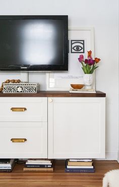 a flat screen tv sitting on top of a wooden dresser next to a white wall