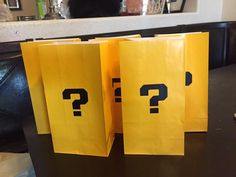 two yellow bags with question marks on them sitting on a table next to a black cat