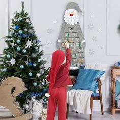 a woman in red pajamas standing next to a christmas tree with decorations on the wall